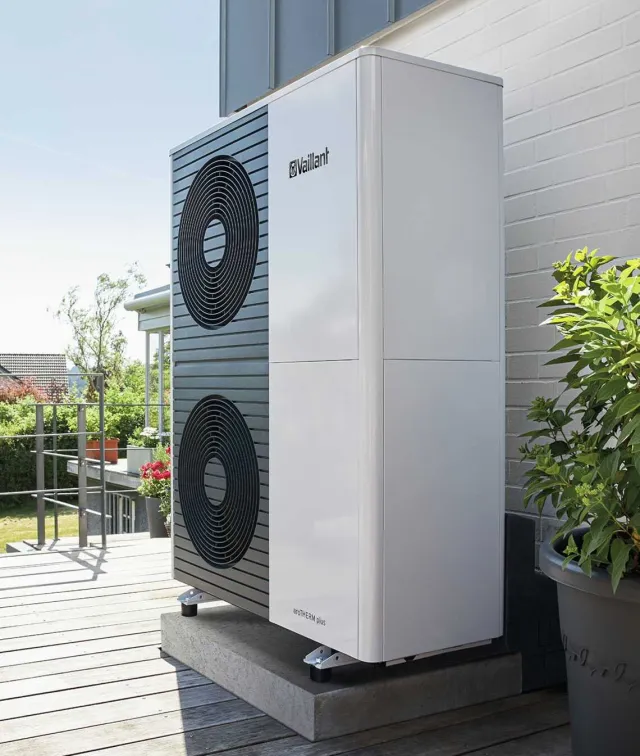 Vaillant air source heat pump outdoor unit on a concrete base beside a white brick wall