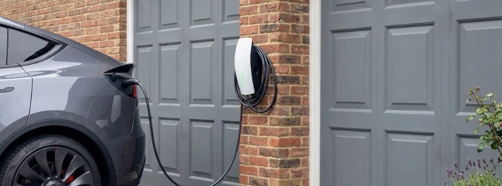 Modern home EV charger on the side of a UK house with a car parked on the driveway
