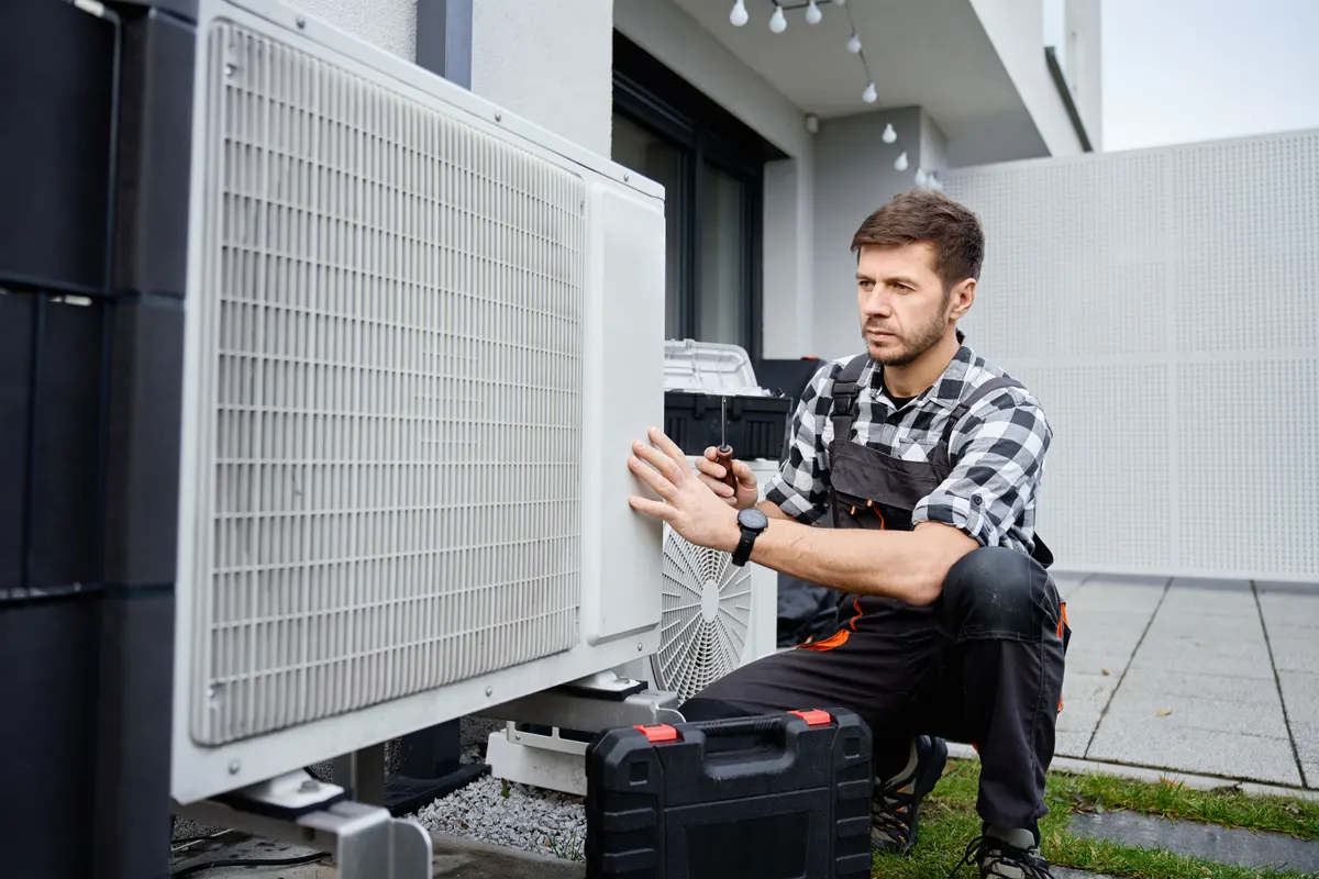 Heating engineer working on an air source heat pump outside a home