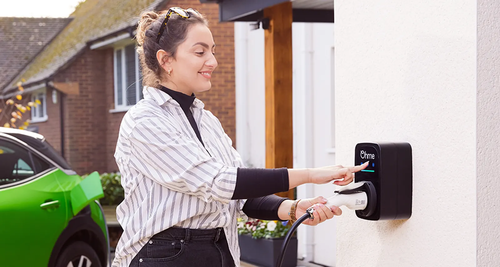 Homeowner plugging a green EV into an Ohme ePod wall charger on a UK driveway