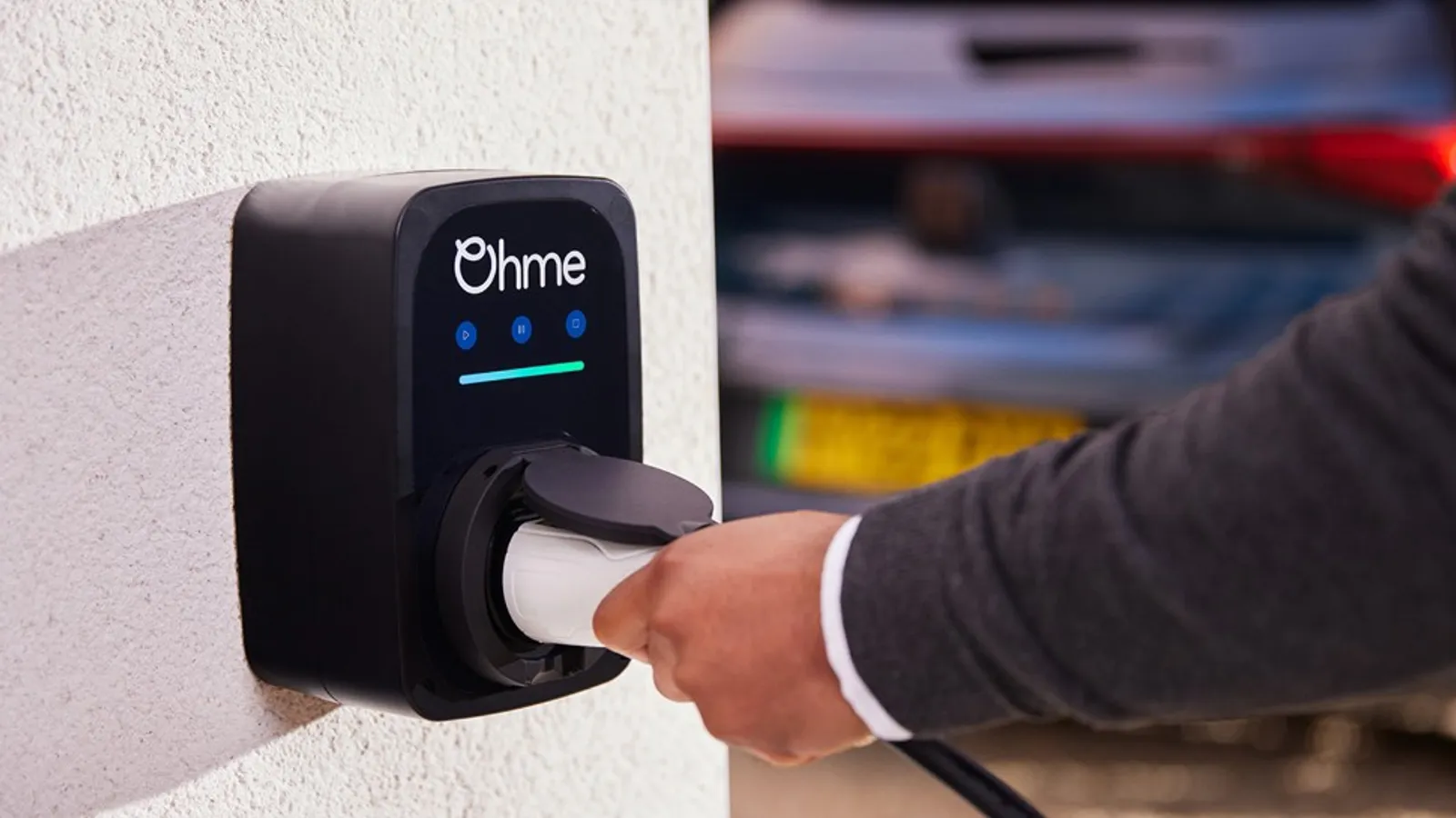 Ohme Home Pro smart EV charger fitted to a UK home wall, with a driver inserting the charging plug into a car