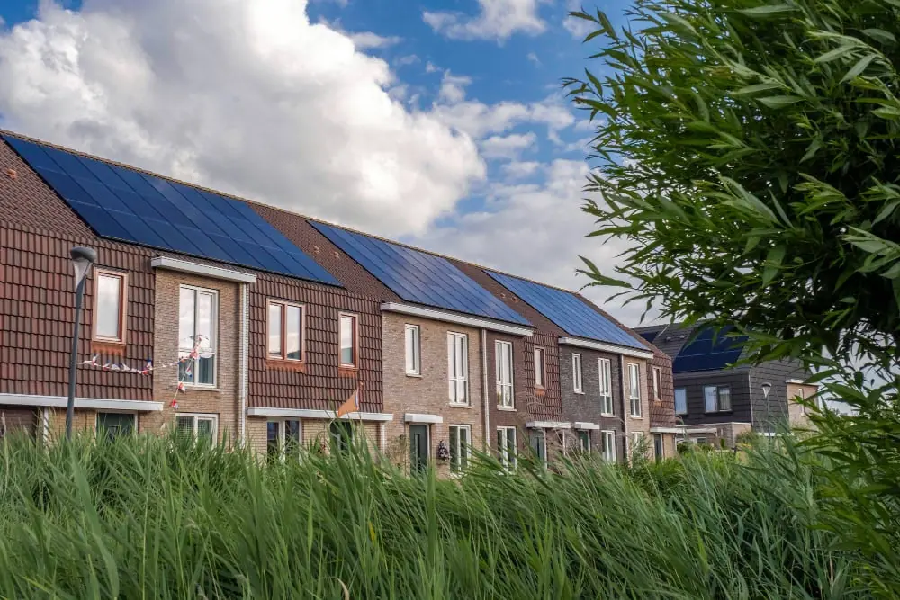 Row of modern UK terrace houses with solar panel arrays on pitched roofs under a partly cloudy sky