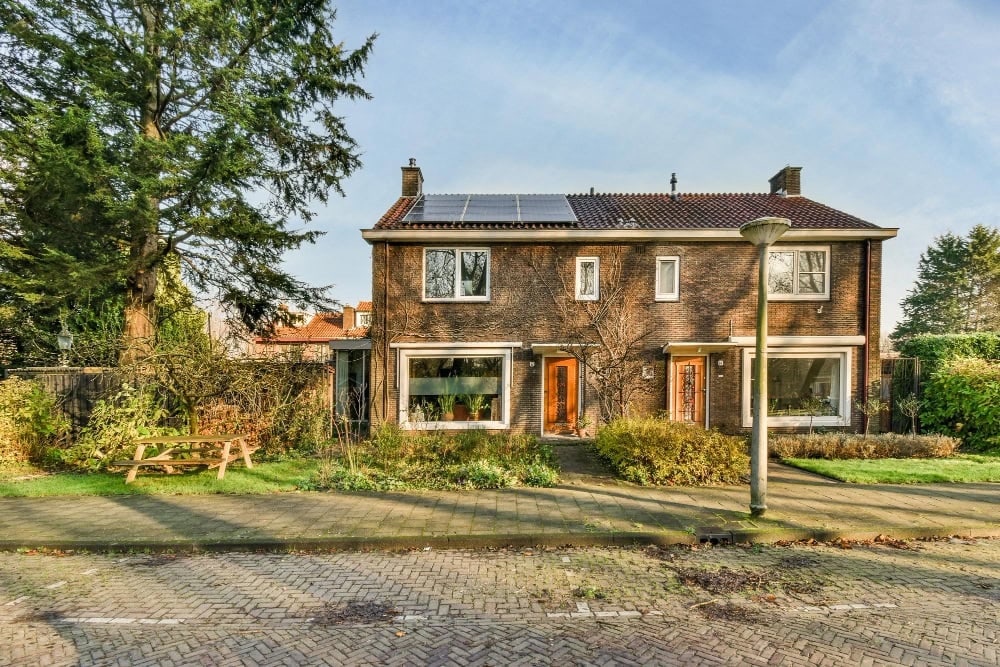 Semi-detached brick house in the UK with solar panels installed on the pitched roof and a front garden