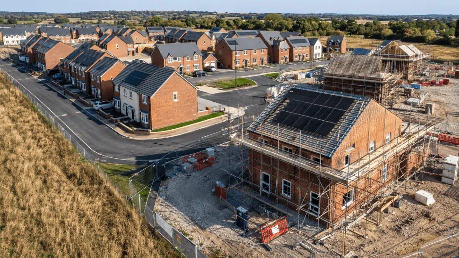 Aerial view of a UK new-build estate with solar panels going on roofs during construction, representing homes being upgraded under the Warm Homes Plan