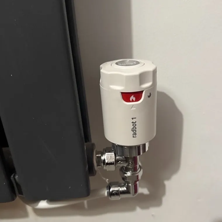 Smart thermostatic radiator valve fitted to a dark grey designer radiator