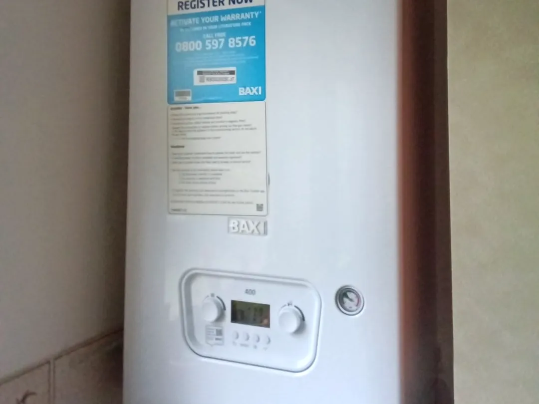 Close-up of a newly fitted Baxi combi boiler, still carrying its register-your-warranty sticker above the controls