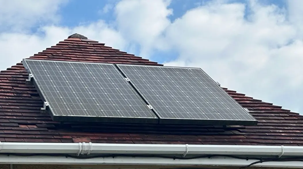 Two solar panels on a hipped tiled roof under a blue sky