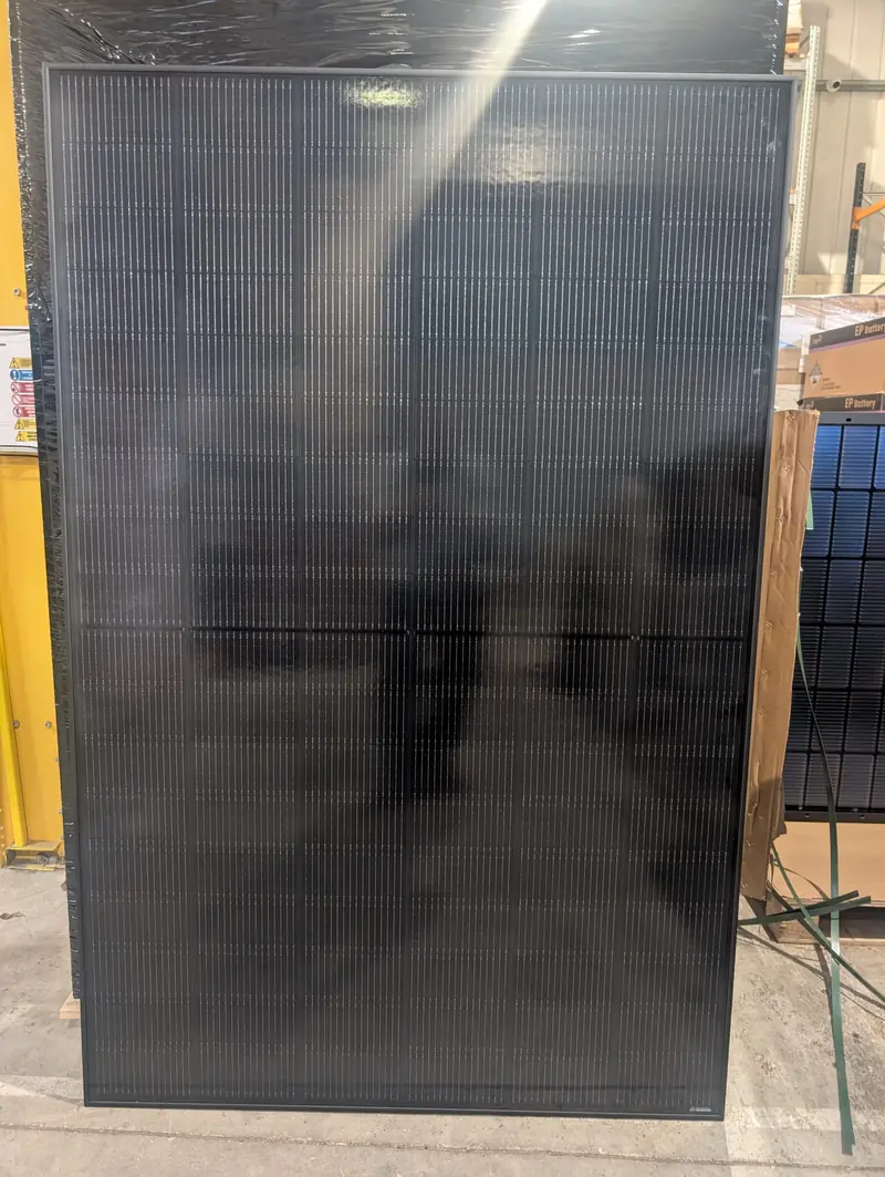 Unboxed all-black solar panel standing upright in a warehouse before delivery