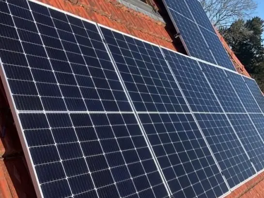 Solar panels on a red-tiled roof beside a roof window, against a clear blue sky