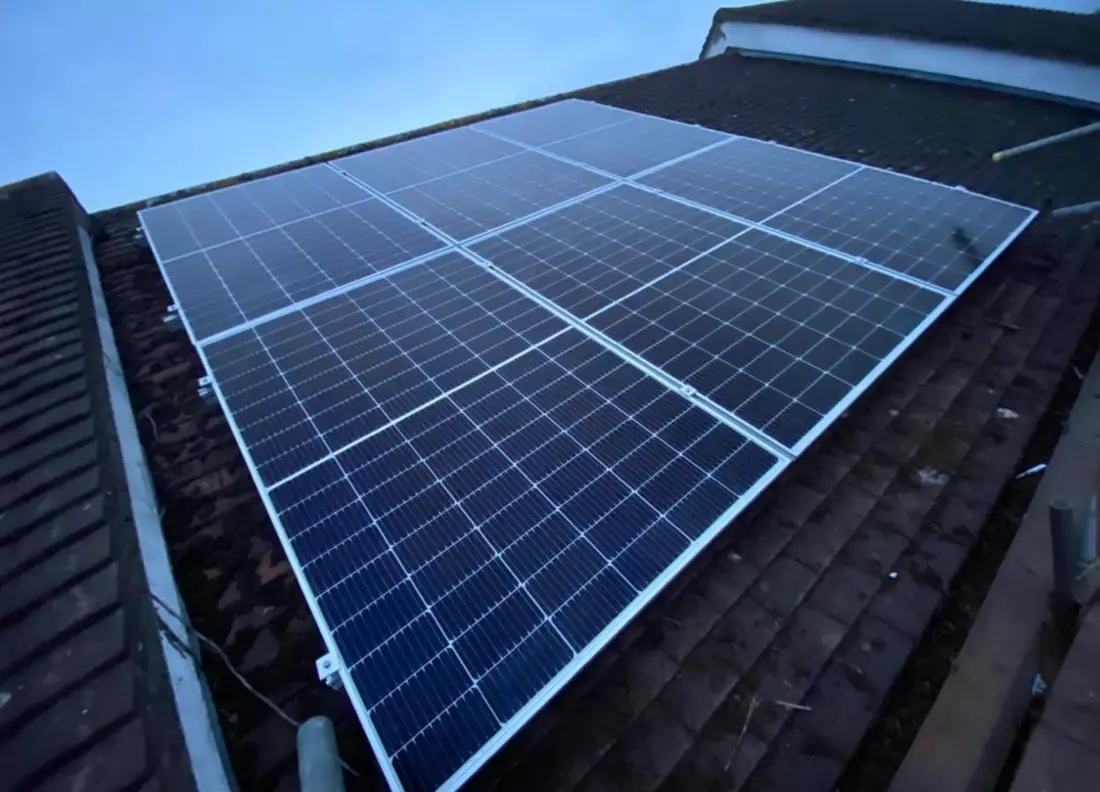 Eight solar panels on a dark tiled roof at dusk