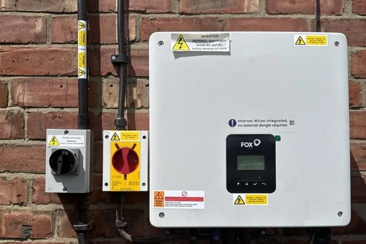 Fox ESS inverter on a brick wall, with its AC and DC isolator switches mounted alongside