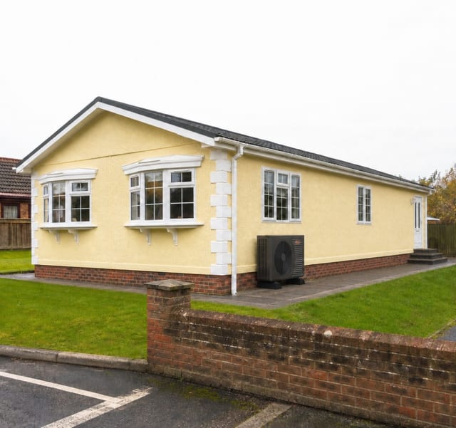Air source heat pump installed on the paved path beside a cream residential park home