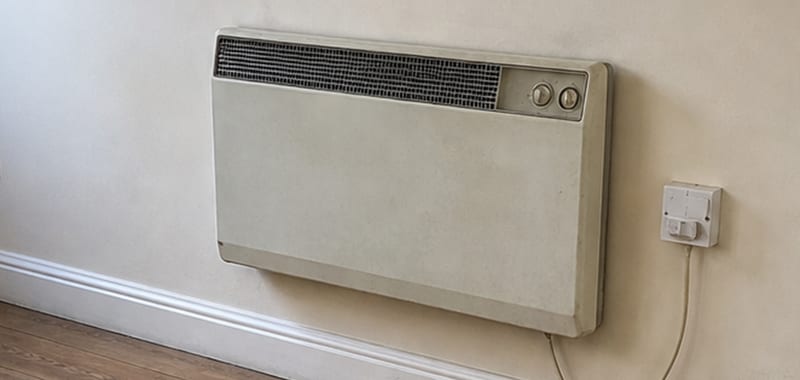Wall-mounted electric radiator with control dials and a fused spur on the wall beside it