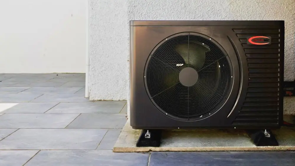 Trianco Activair air source heat pump on a patio beneath a vine-covered white wall