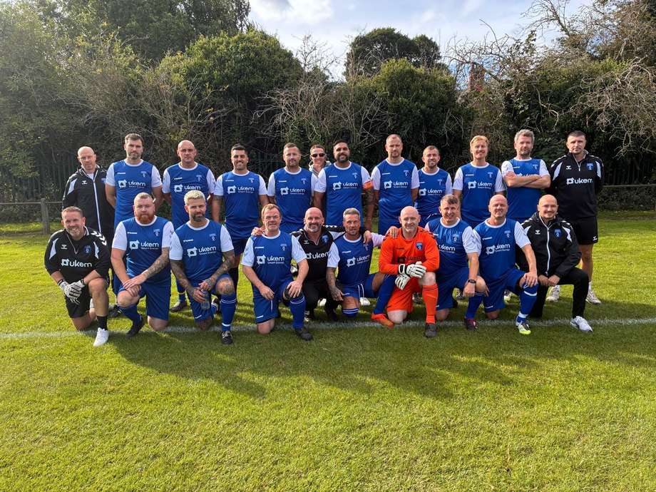 Adult grassroots football team in blue UKEM-sponsored kits lined up on a grass pitch
