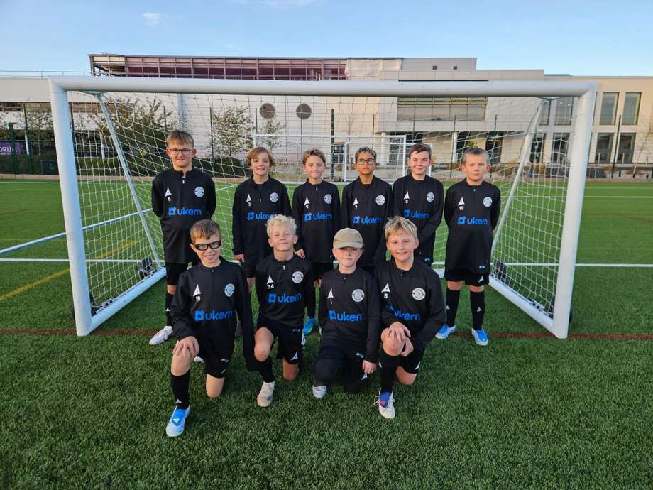 Children's football team in black UKEM-sponsored kits in front of a goal on an all-weather pitch
