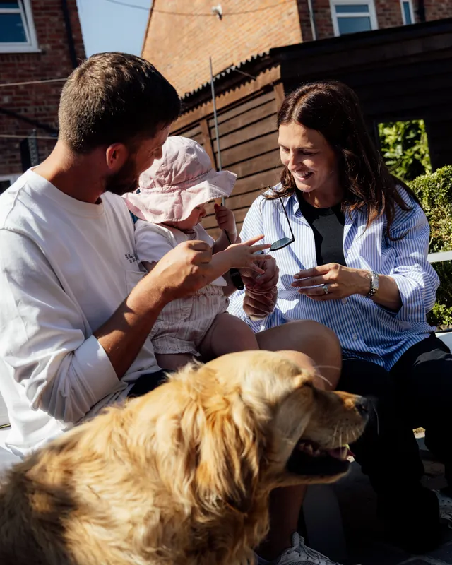 Sophie, her partner and their baby relaxing in the garden with their golden retriever