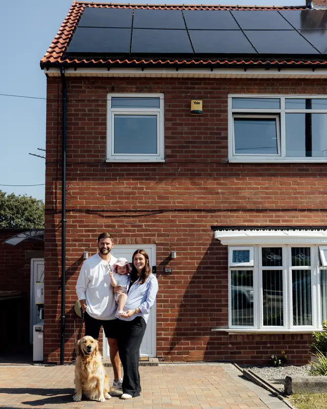 Family and their golden retriever outside their brick semi with new black solar panels on the roof